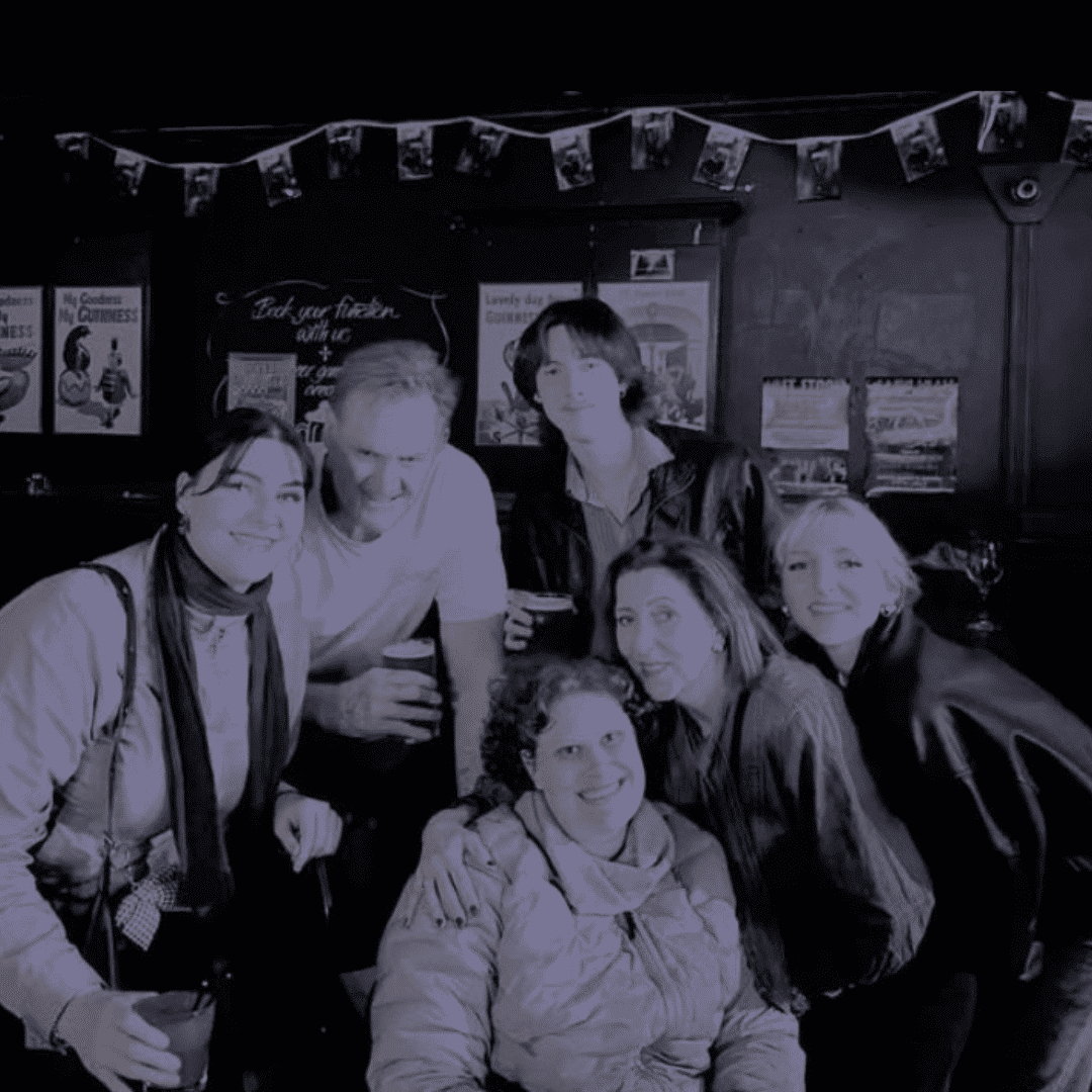 A gang of friends in their 20s smile at the camera. One woman is seated in a wheelchair.