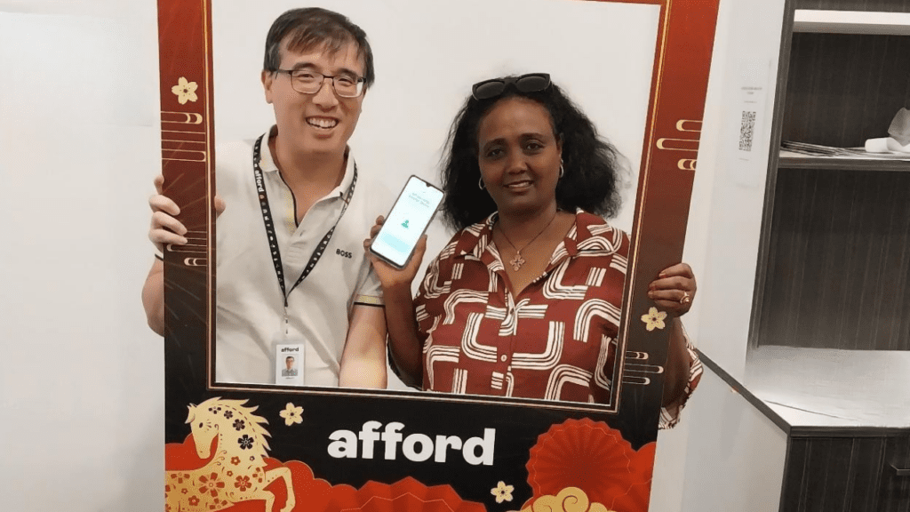 A man and a woman smile broadly at the camera while holding an oversize frame in which they stand.